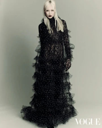 Editorial fashion portrait of an adult female with platinum blonde hair wearing a ruffled black lace gown in a photo studio.