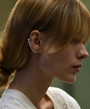 Close-up profile of a woman wearing pearl and gold ear cuffs and a white textured knit top for an editorial shoot.