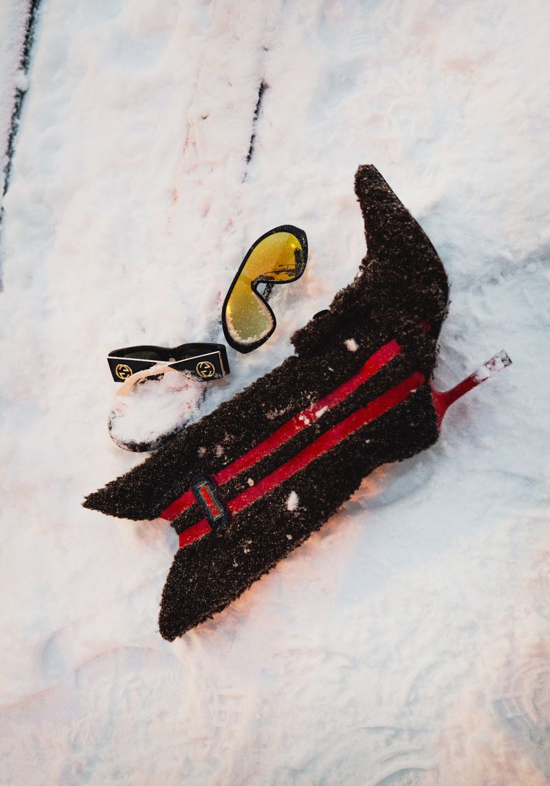 Ski equipment including a ski, ski goggles and ski mask in the snow. The ski is black with red stripes. The ski mask is black with a gold emblem.