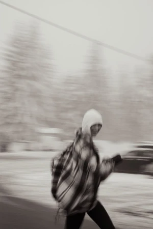 Motion-blurred photo of a person wearing a plaid jacket and hood walking outdoors in a snowy landscape
