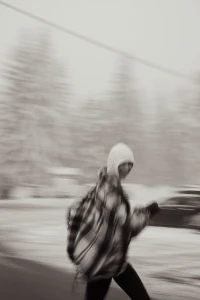 Motion-blurred photo of a person wearing a plaid jacket and hood walking outdoors in a snowy landscape