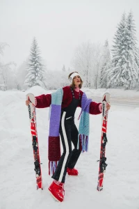 Model in red sweater and black ski pants holding two skis in a snowy forest landscape for L'Officiel Argentina