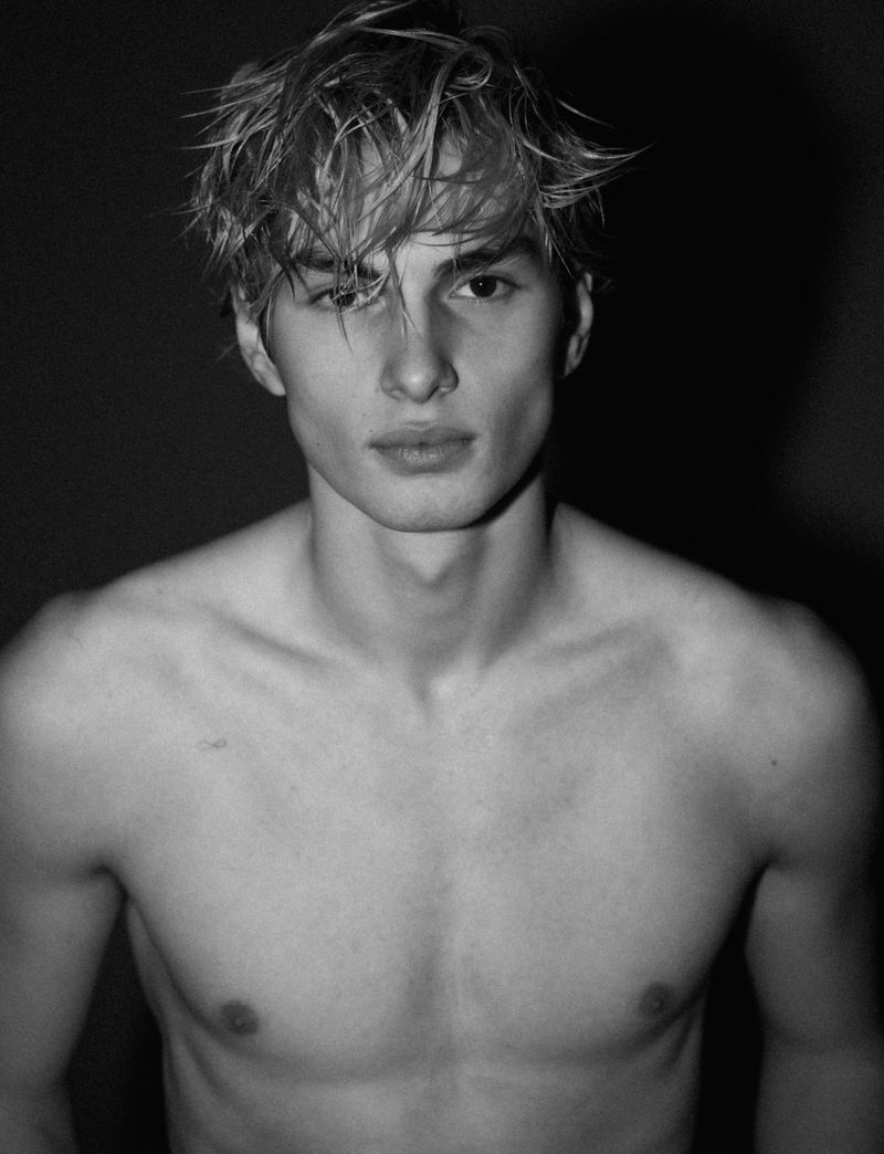 Portrait of a young shirtless male model with wet tousled hair against a dark background for HERO Magazine.