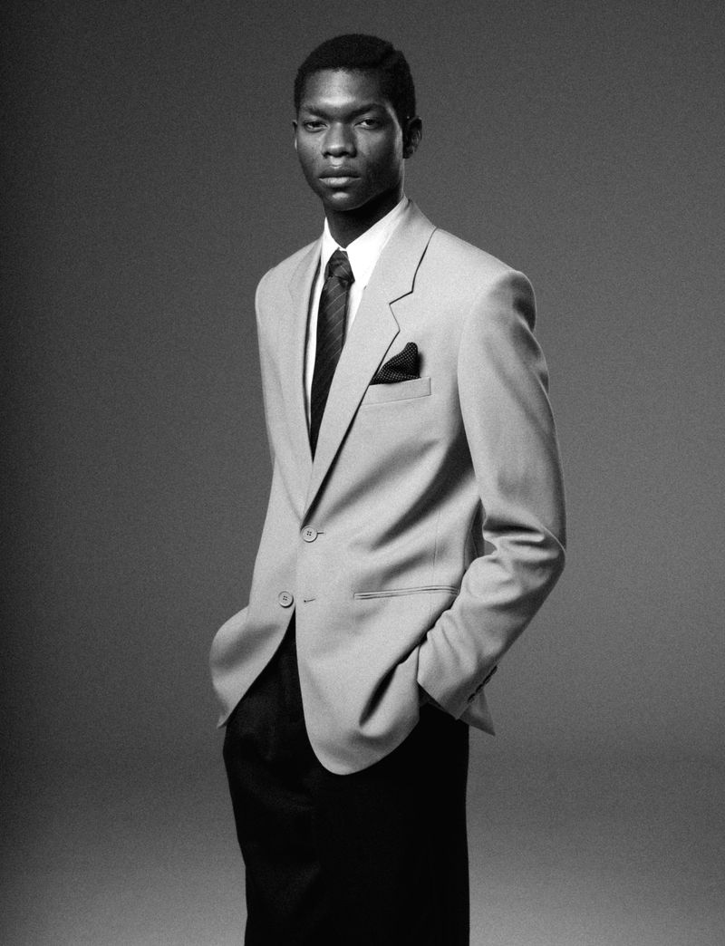 Portrait of an African American man in a gray suit, black tie, and black pocket square against a simple gray gradient background.