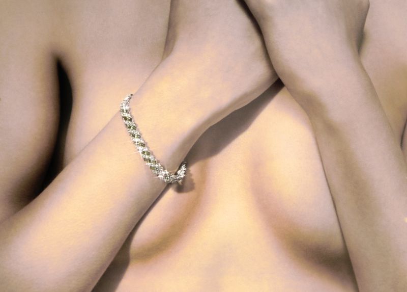 Close-up of a woman with light skin and a sparkly beaded bracelet on her arm, posing indoors with a soft, romantic lighting effect.