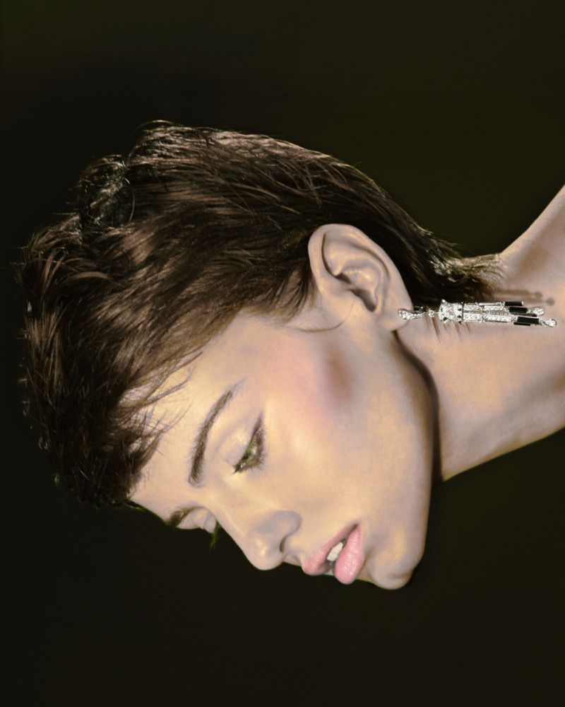 Artistic image of a woman with a silver object connected to her ear against a dark background, head tilted downward.