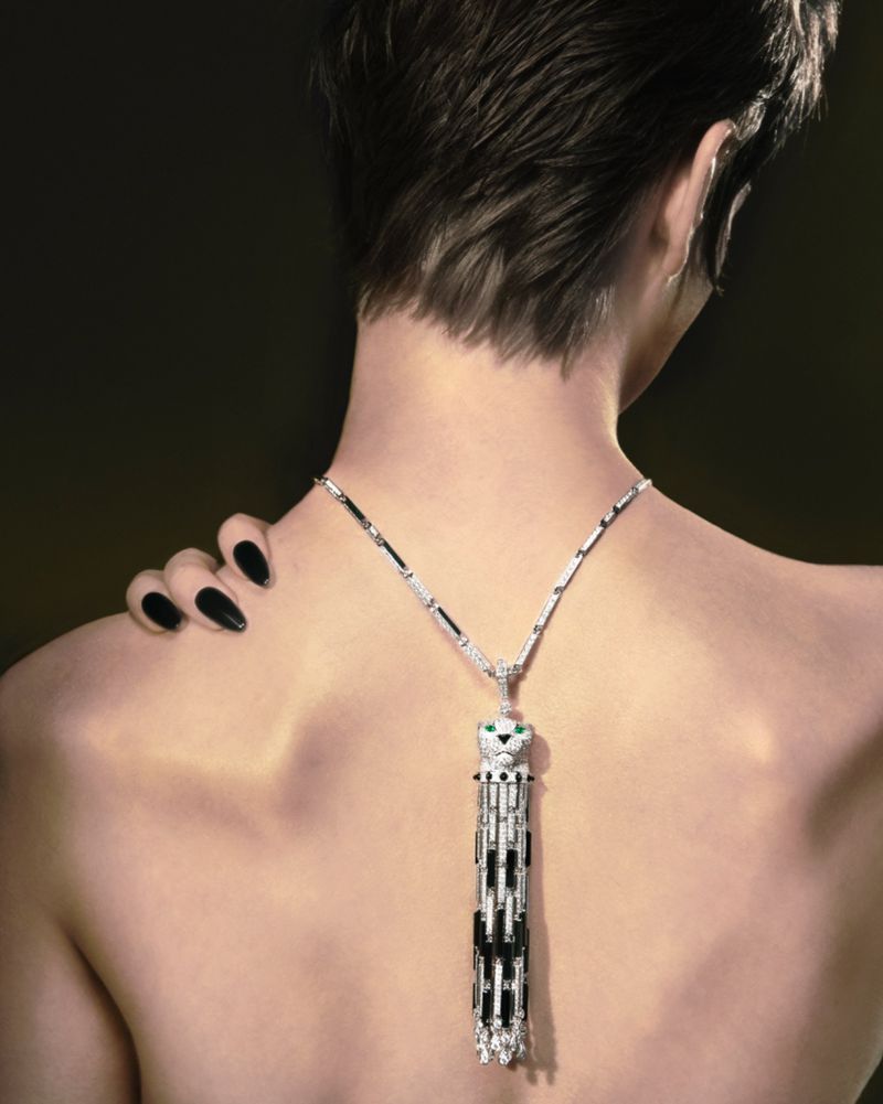 Back view of a fair-skinned woman with a pixie cut wearing a silver necklace with a decorative cat pendant, against a dark background.