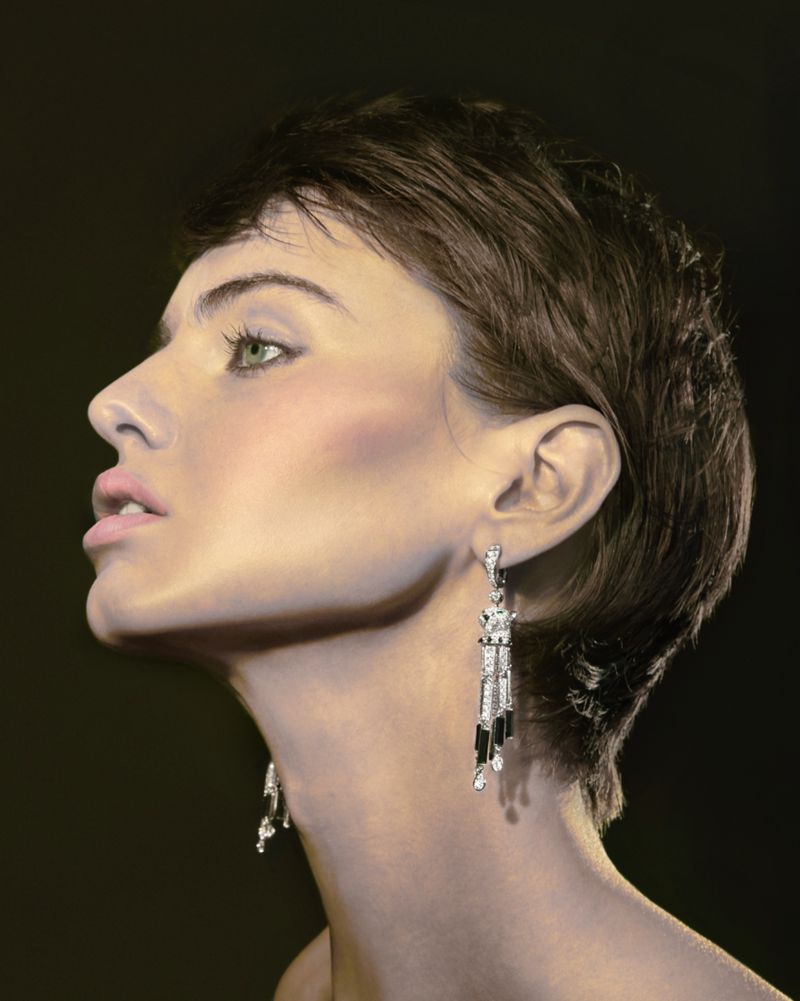 Portrait of an adult woman with short brown hair, wearing dangling earrings and looking up against a dark background. Beauty shot, head and shoulders.