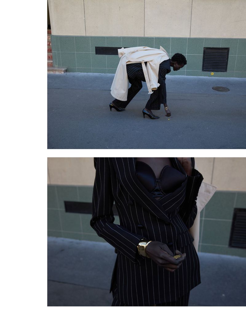 A Black model in a pinstripe suit and cream coat poses on a city street in high heels, with a close-up of the suit revealing a gold bracelet.