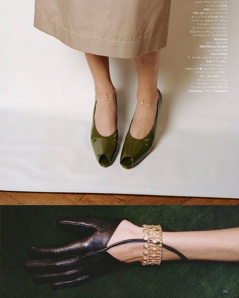 Close-up fashion shot of feet in glossy peep-toe heels with ankle bracelets, plus gloved hand with bracelet, on white and wood.