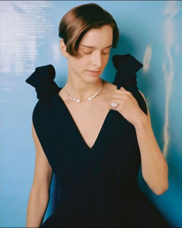 Woman in black dress poses in front of a blue background, showcasing a silver necklace and ring with a serious expression.