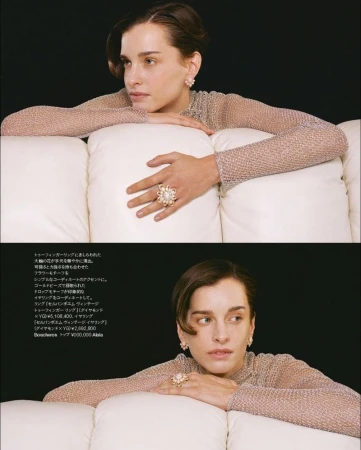 Fashion shot of a woman with short brown hair wearing large pearl earrings and a large pearl ring while resting on a white sofa.