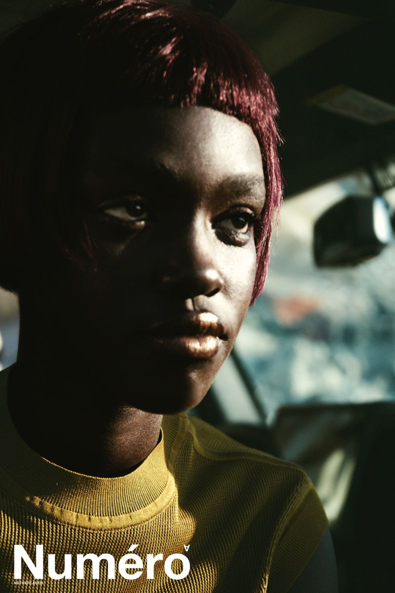 Close-up portrait of model Alek Deng with reddish-brown hair and metallic lipstick seated inside a car for Numero Netherlands