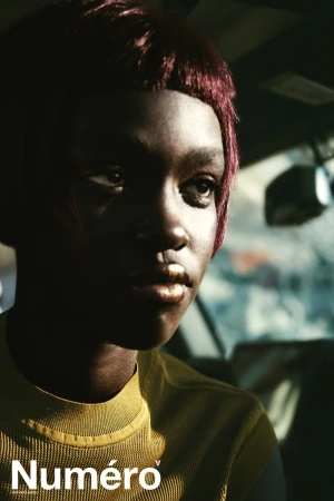 Close-up portrait of model Alek Deng with reddish-brown hair and metallic lipstick seated inside a car for Numero Netherlands