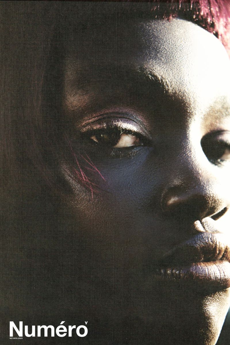 Close-up portrait of an African American woman with textured skin and short reddish hair. Dramatic light emphasizes the face.