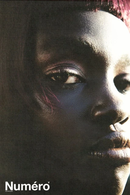 Close-up portrait of an African American woman with textured skin and short reddish hair. Dramatic light emphasizes the face.