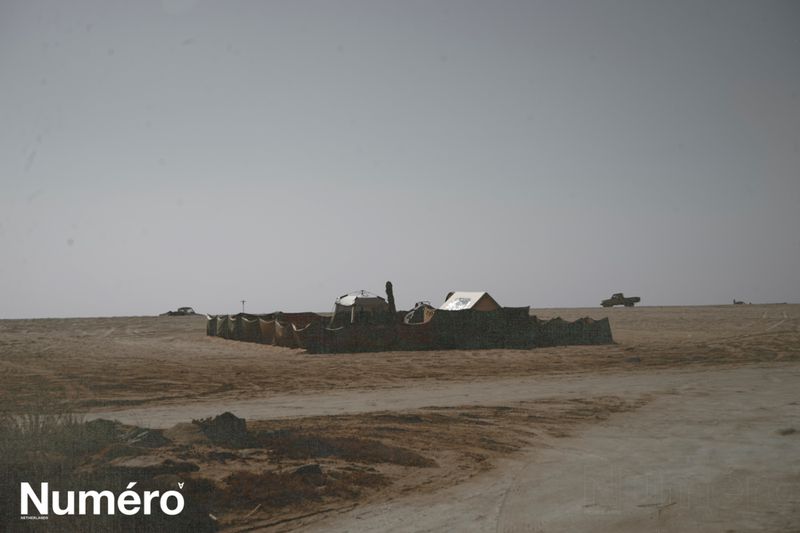 Desert landscape featuring an abstract structure, with a truck in the distance under a clear sky, and the 'Numero' logo visible.