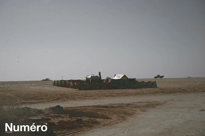 Desert landscape featuring an abstract structure, with a truck in the distance under a clear sky, and the 'Numero' logo visible.