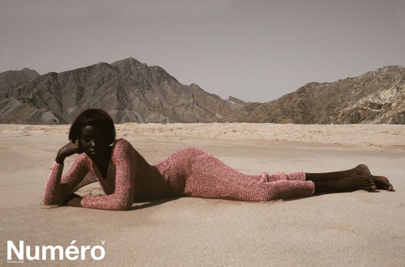 A woman in a pink dress lies on a sandy beach in front of mountains in a fashion editorial, with 'Numero' magazine logo.