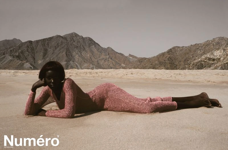 A woman in a pink dress lies on a sandy beach in front of mountains in a fashion editorial, with 'Numero' magazine logo.