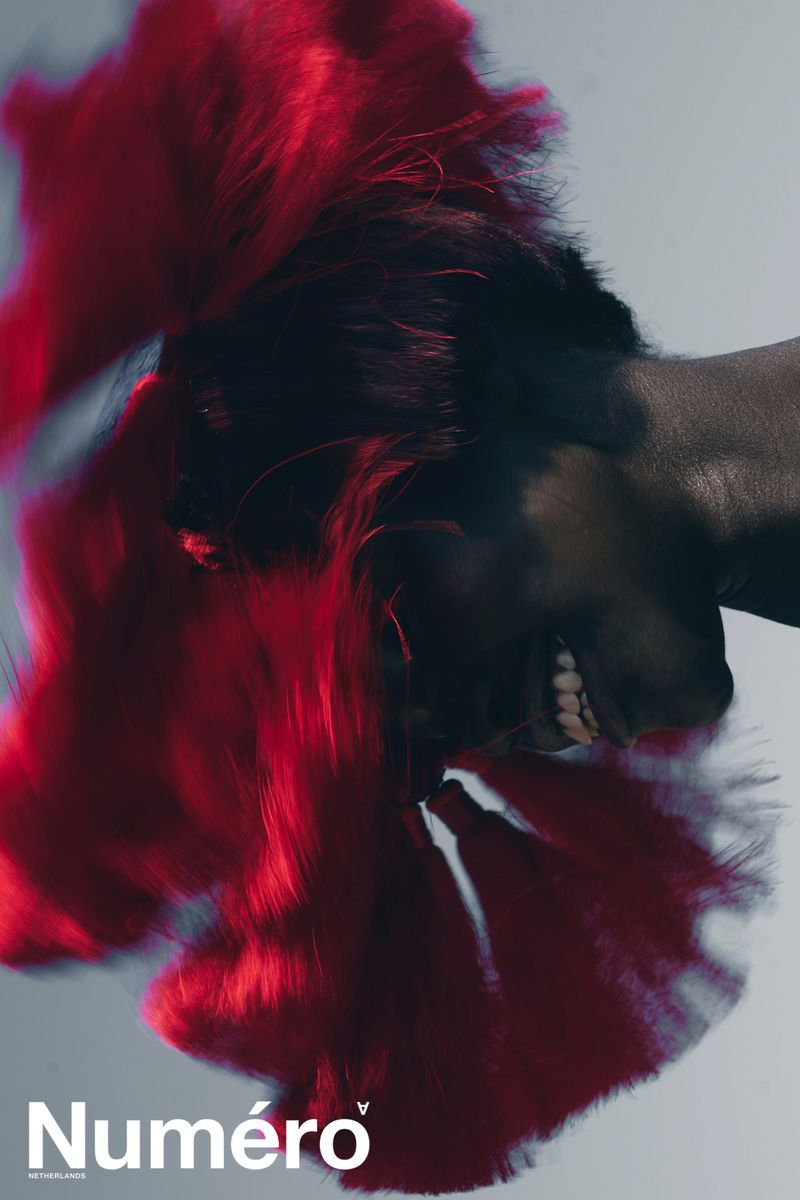 Fashion magazine cover featuring a dark-skinned person with bright red hair against a pale background, displaying beauty and style.
