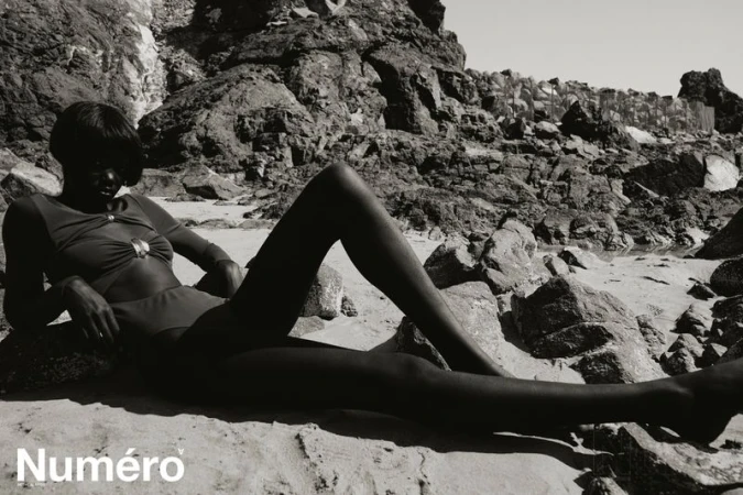 Model Alek Deng posing on a rocky shore in a monochrome fashion editorial for Numero Netherlands by Bruno Unikowsky.