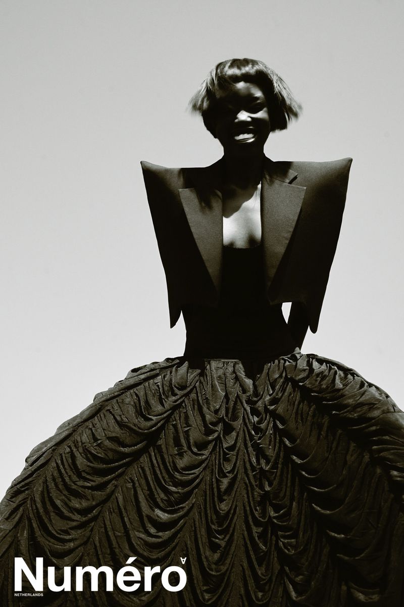 Model Alek Deng in a structured black blazer and voluminous ballgown skirt against a pale background for Numero Netherlands.