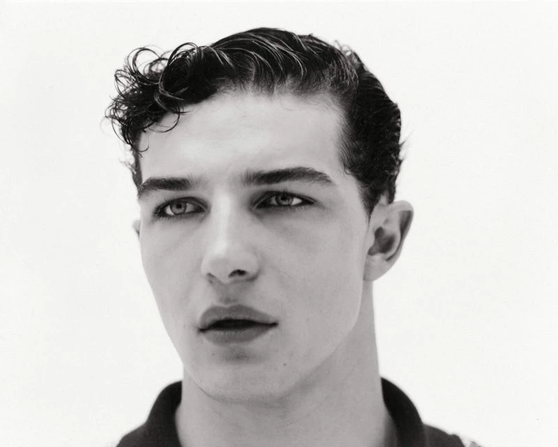 Black and white portrait of a young adult male with dark curly hair, fair skin, and dark eyes, posing against a plain white background.