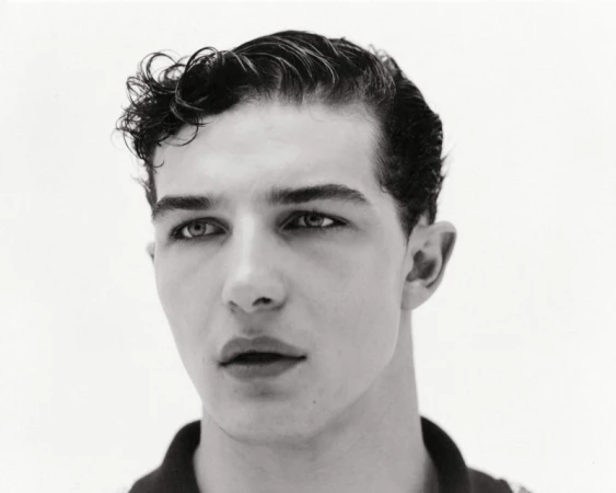 Black and white portrait of a young adult male with dark curly hair, fair skin, and dark eyes, posing against a plain white background.