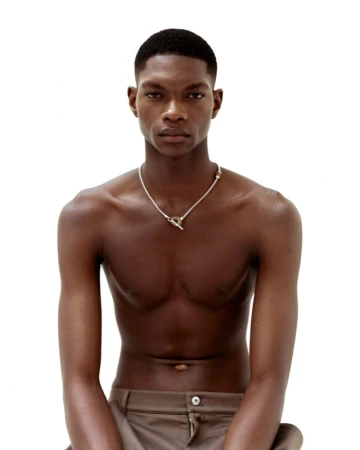 Portrait of a shirtless young Black man wearing a silver toggle necklace against a clean white background