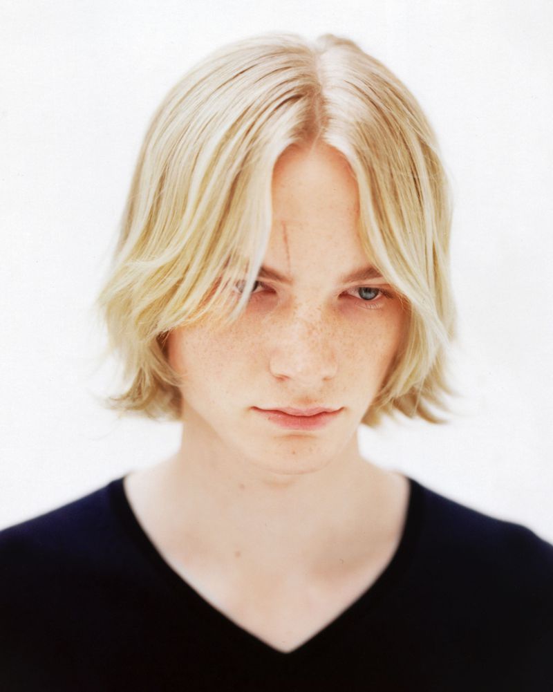 Portrait of a young adult with blond hair and a black shirt against a white backdrop, capturing a close-up view.