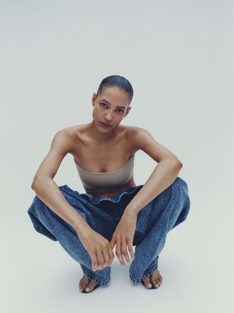 Model crouching wearing a bandeau top and loose denim jeans against a seamless white background.
