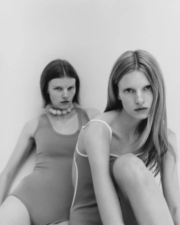 Two female models in fitted swimsuits posing against a neutral white background in a studio setting.