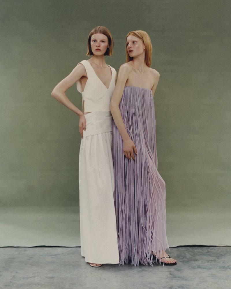 Two female models posing in cream and lilac dresses against an olive green studio backdrop