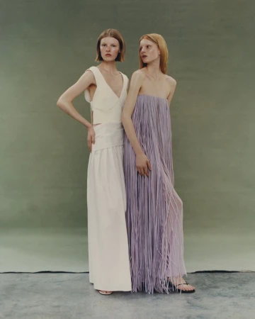 Two female models posing in cream and lilac dresses against an olive green studio backdrop