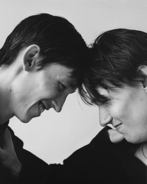 Black and white portrait of a smiling couple touching foreheads, creating an intimate, tender moment in a simple photo studio setting.