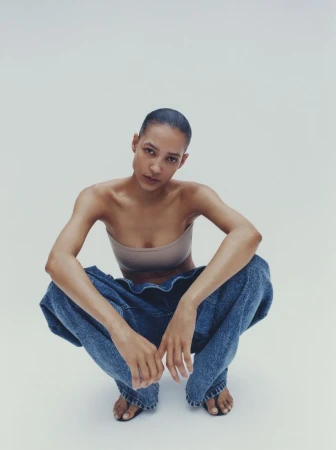 Model crouching wearing a bandeau top and loose denim jeans against a seamless white background.