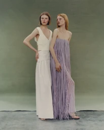 Two female models posing in cream and lilac dresses against an olive green studio backdrop