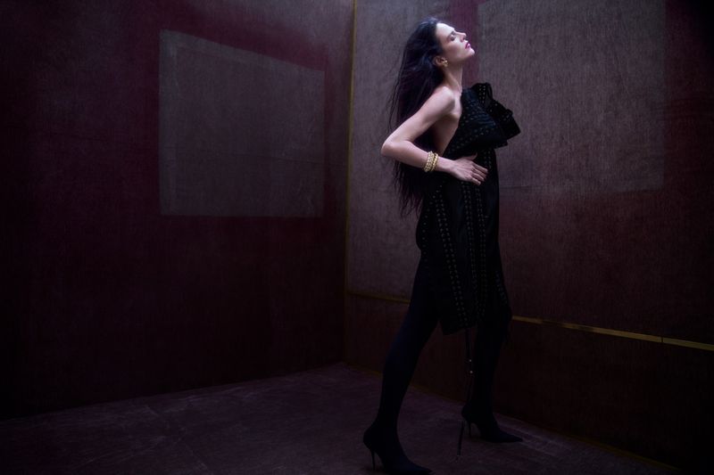 Model Aymeline Valade wearing a black textured dress in a dark moody studio space for Present Space