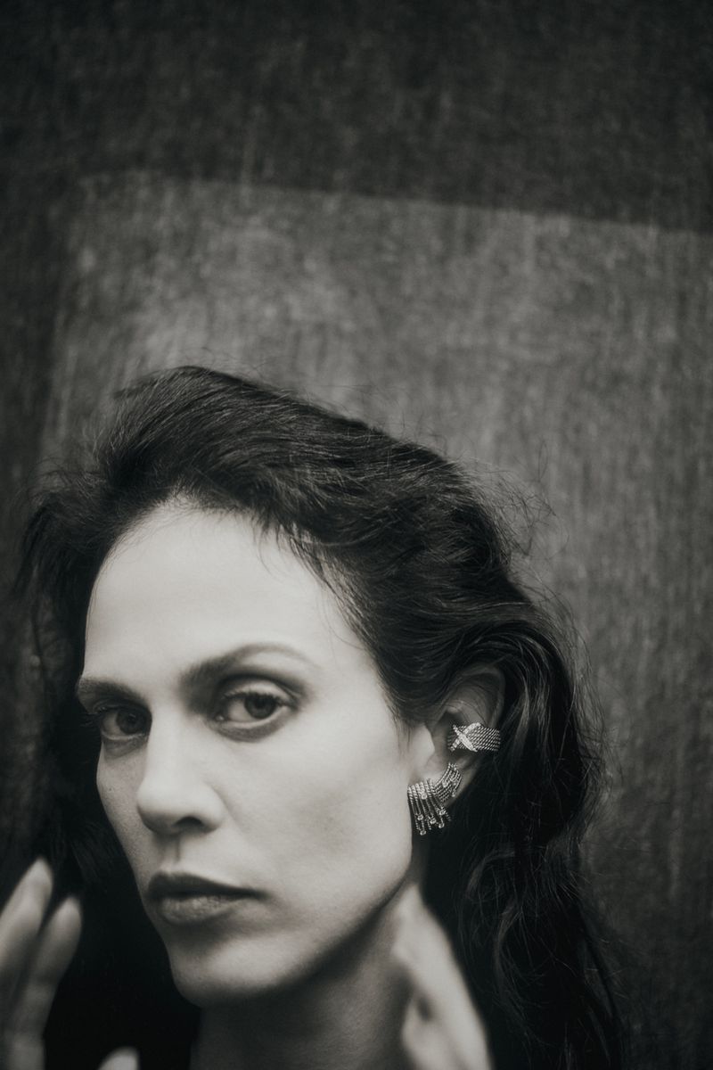 Close-up monochrome portrait of model Aymeline Valade wearing diamond earrings against a textured dark background