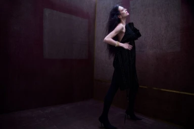 Model Aymeline Valade wearing a black textured dress in a dark moody studio space for Present Space