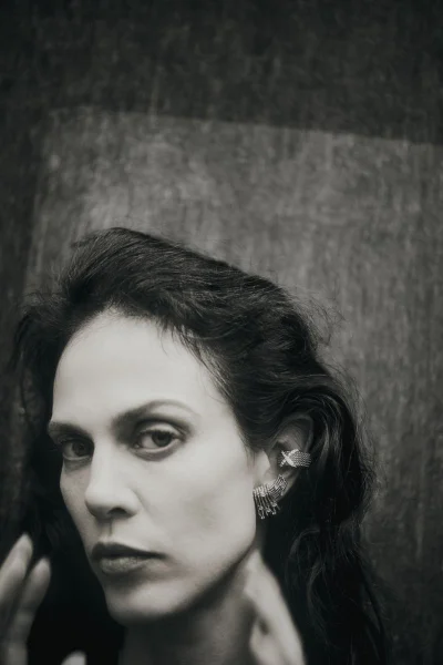 Close-up monochrome portrait of model Aymeline Valade wearing diamond earrings against a textured dark background