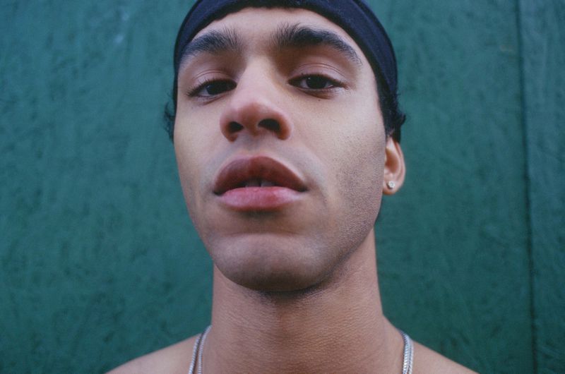 Close-up portrait of a young man wearing a black headband against a green textured background for En Familia.