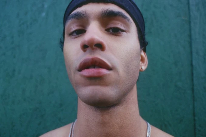 Close-up portrait of a young man wearing a black headband against a green textured background for En Familia.