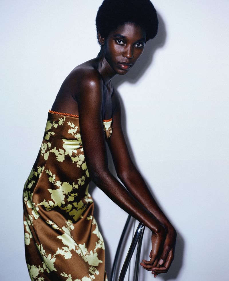 Elegant Black woman in a floral dress posing indoors. Fashion shot with a white background and chrome chair.
