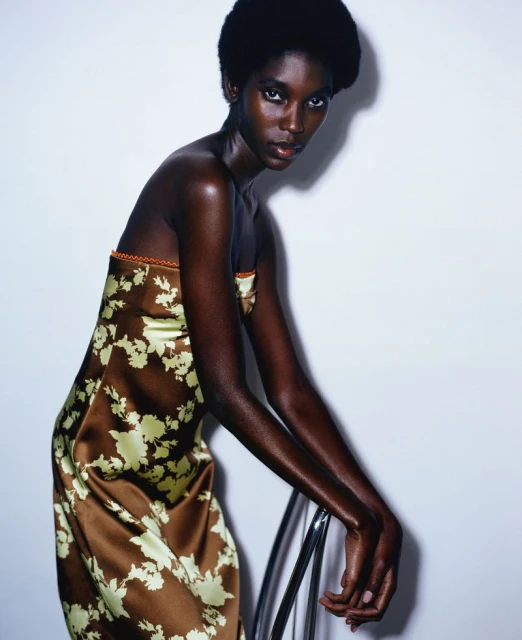 Elegant Black woman in a floral dress posing indoors. Fashion shot with a white background and chrome chair.