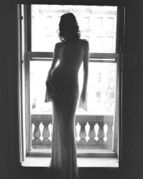 Model standing in silhouette against a bright multi-pane window wearing a long dress for Present Space