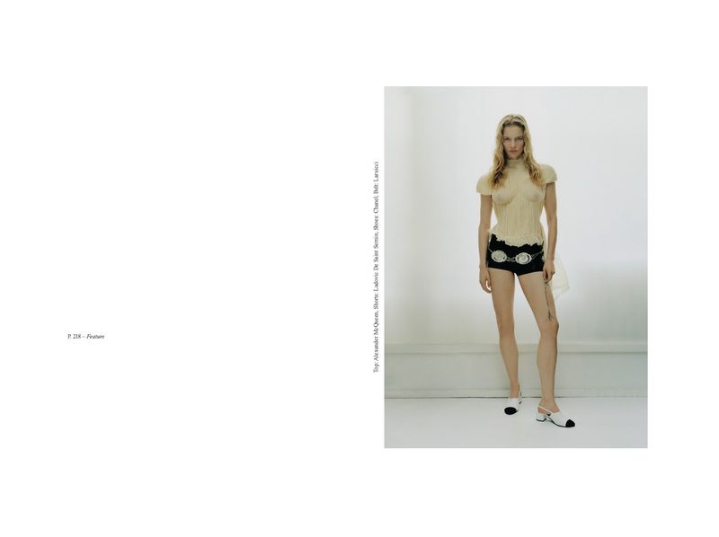 Fashion editorial shot of a model in a cream-colored knit top and black shorts with white and black heels in a bright photo studio.