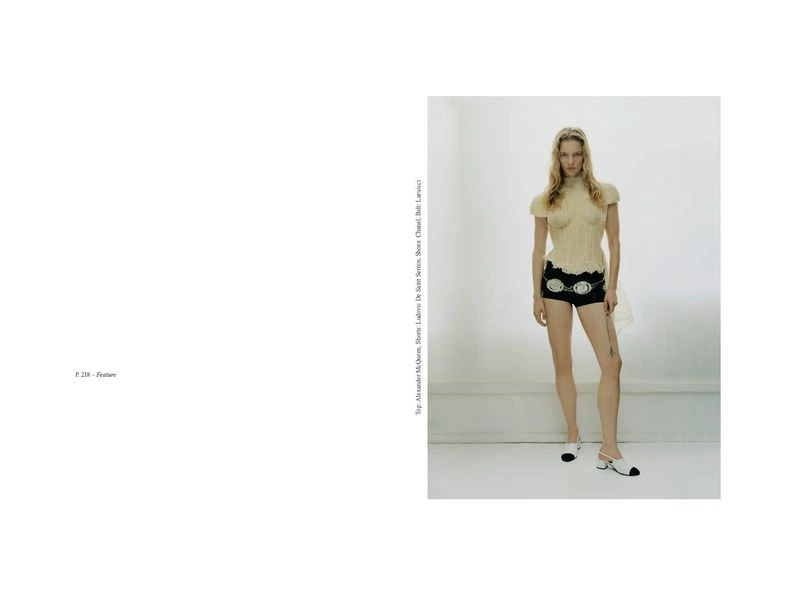 Fashion editorial shot of a model in a cream-colored knit top and black shorts with white and black heels in a bright photo studio.