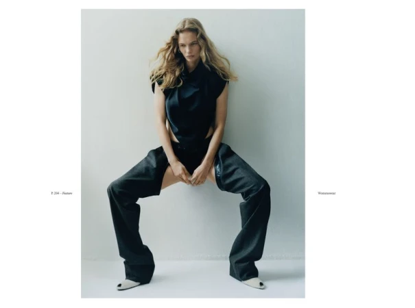 Model in dark sleeveless top and wide trousers posing against a seamless white studio background